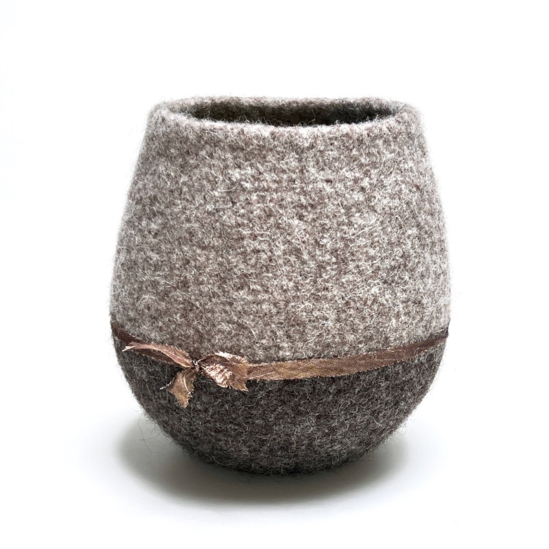 BOLA Bow is a medium hand felted urn in putty and gunmetal colored wool with a rough edged bronze silk trimfrom zed handmade
